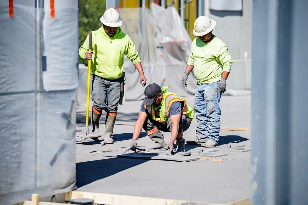 Crew of three concrete finishers in hard hats working on fresh concrete at a commercial plaza