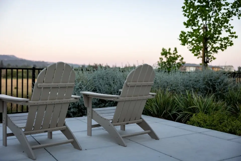 Two outdoor chairs on a smooth gray concrete patio at dusk with landscaping and hills beyond