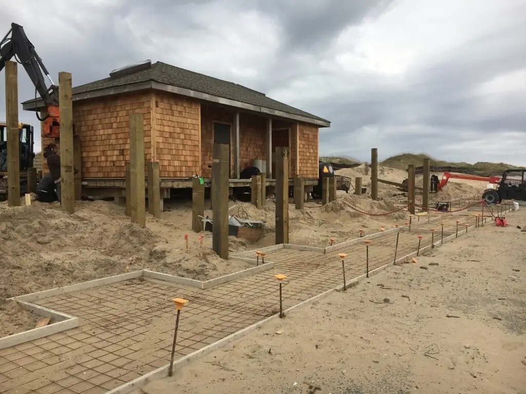 Wooden forms, stakes and reinforcement laid out on prepared ground for a new concrete walkway beside a small building