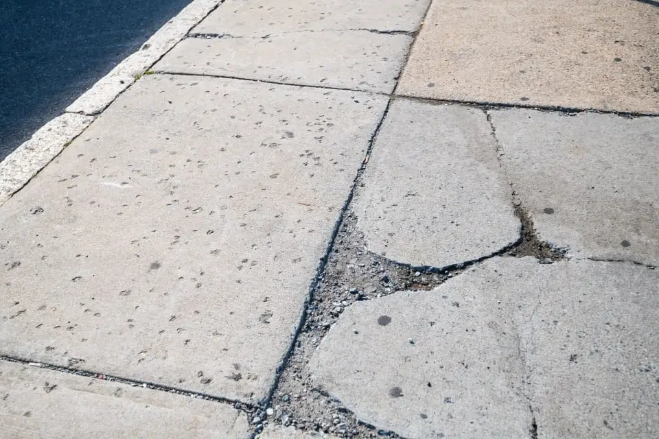 Concrete sidewalk panels with several cracks and a broken, uneven section near a joint