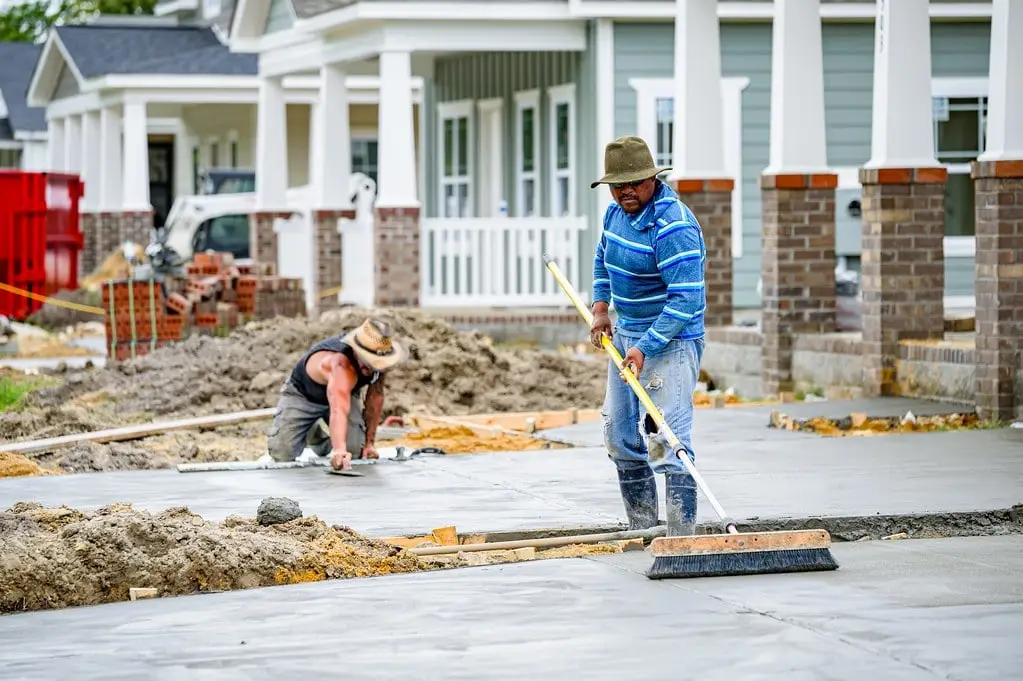 Workers finishing freshly placed concrete in front of a row of new homes