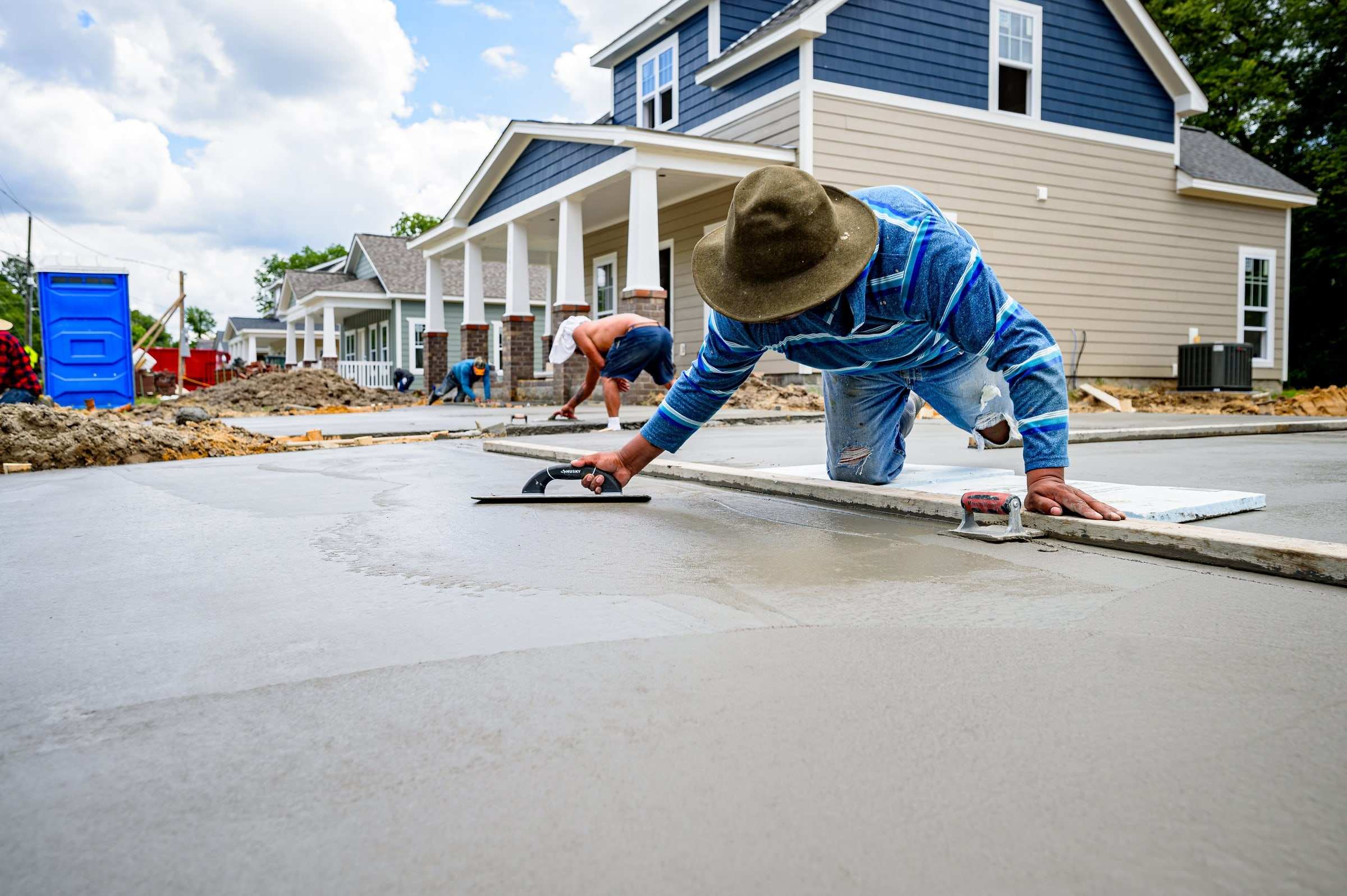 Concrete finisher smoothing a freshly poured slab in front of a row of new homes
