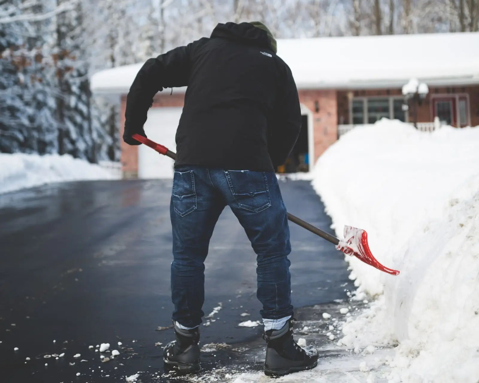 Person shoveling snow from a residential driveway beside a tall snowbank after a winter storm